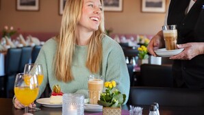 Escena en un restaurante con una mesa para dos, que incluye un postre, un vaso de zumo de naranja y un vaso de café.