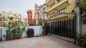 A courtyard with a black gate, potted plants, and a concrete floor. - Le Rhododendron Chambres D'hotes (Kathmandu)