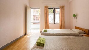 A room with two beds, a wooden floor, a window with curtains, and a green lamp on the wall. - Le Rhododendron Chambres D'hotes (Kathmandu)