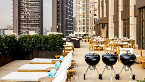 A rooftop dining area with outdoor seating, including lounge chairs and tables, and three barbecue grills. - Residence G Shenzhen (Shenzhen)