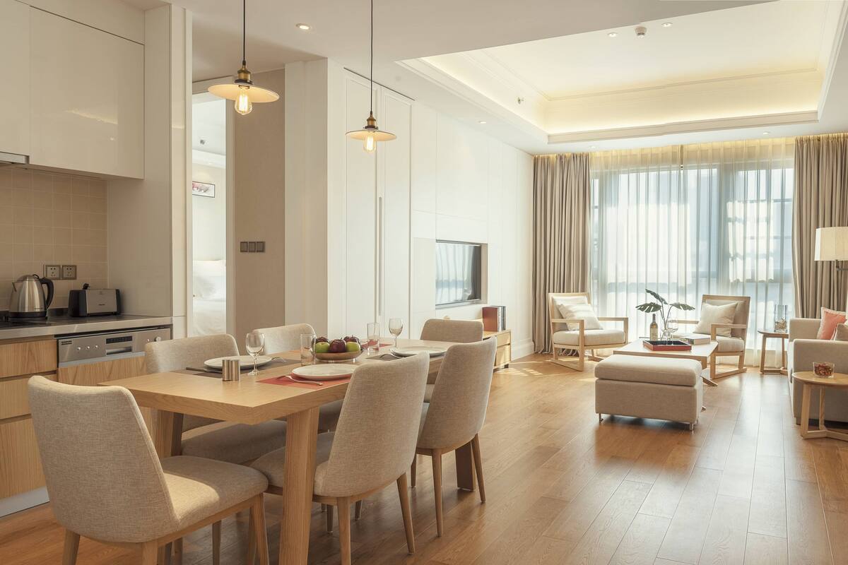A modern hotel room with a dining area, a living area with a sofa and armchairs, and a kitchen.