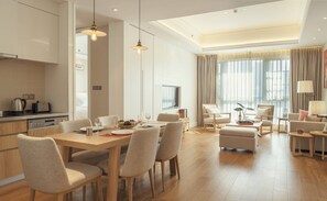 A modern hotel room with a dining area, a living area with a sofa and armchairs, and a kitchen.