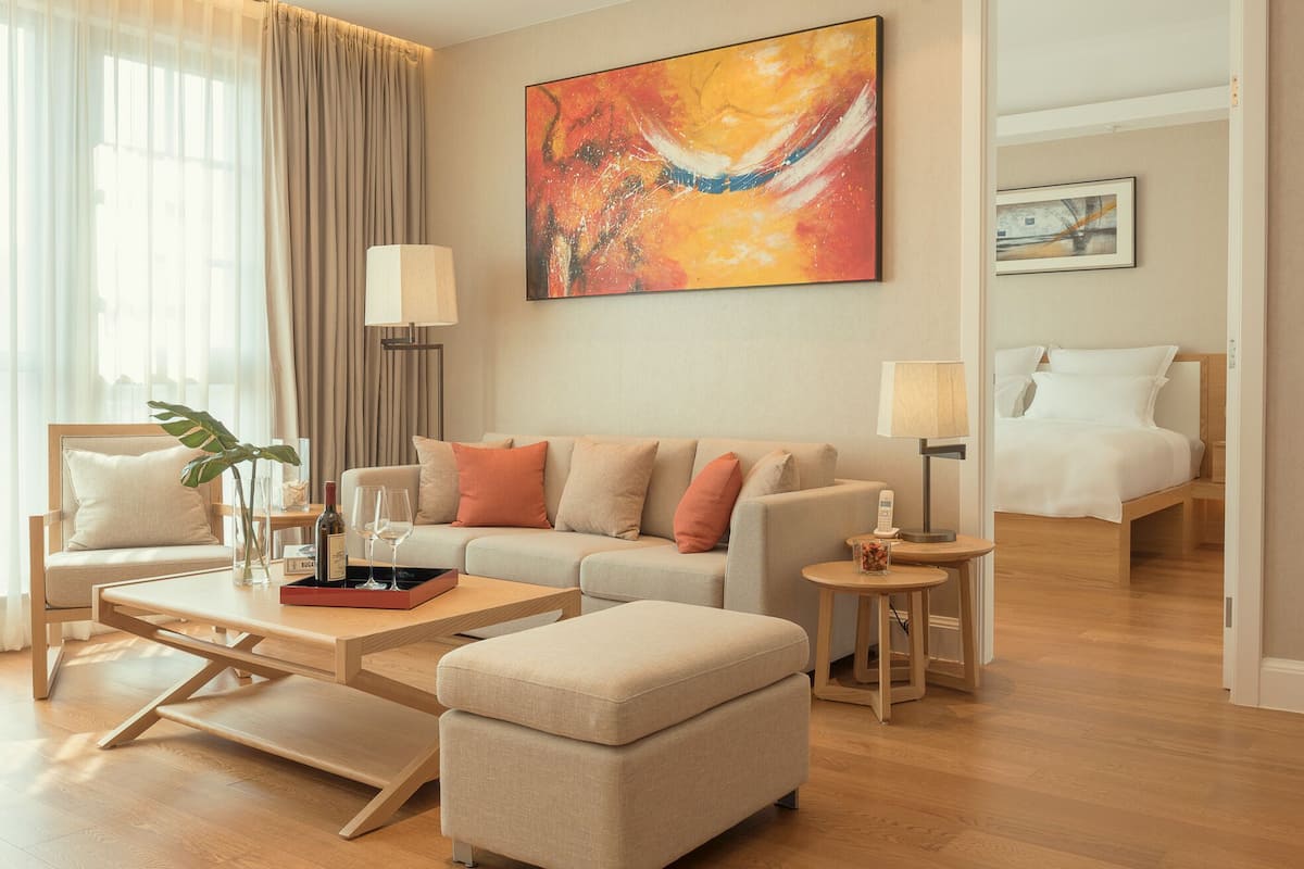 A modern hotel room with a sofa, ottoman, coffee table, and a bed.