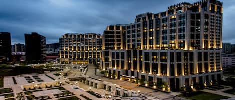 Un moderno edificio de gran altura con fachada simétrica, varios pisos y un patio central con senderos y zonas de estar.