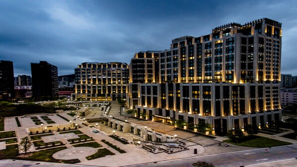 A modern high-rise building with a symmetrical facade, multiple floors, and a central courtyard with pathways and seating areas.