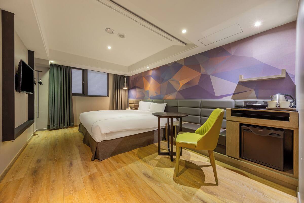 A hotel room with a bed, a desk, a chair, a television, and a wall with geometric patterns.