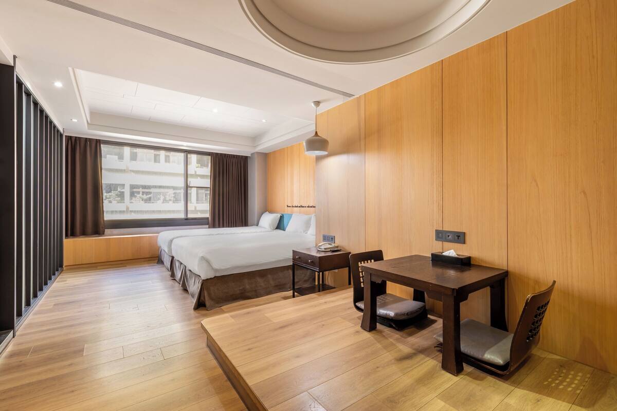 A hotel room with a large bed, a wooden dining table, and a window with curtains.