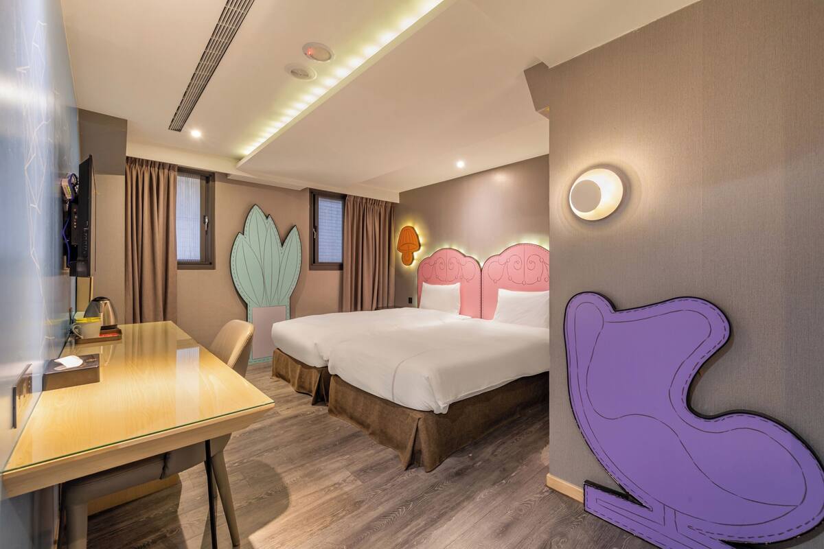 A hotel room with a wooden desk, two beds, a large wall decoration, and a purple chair.