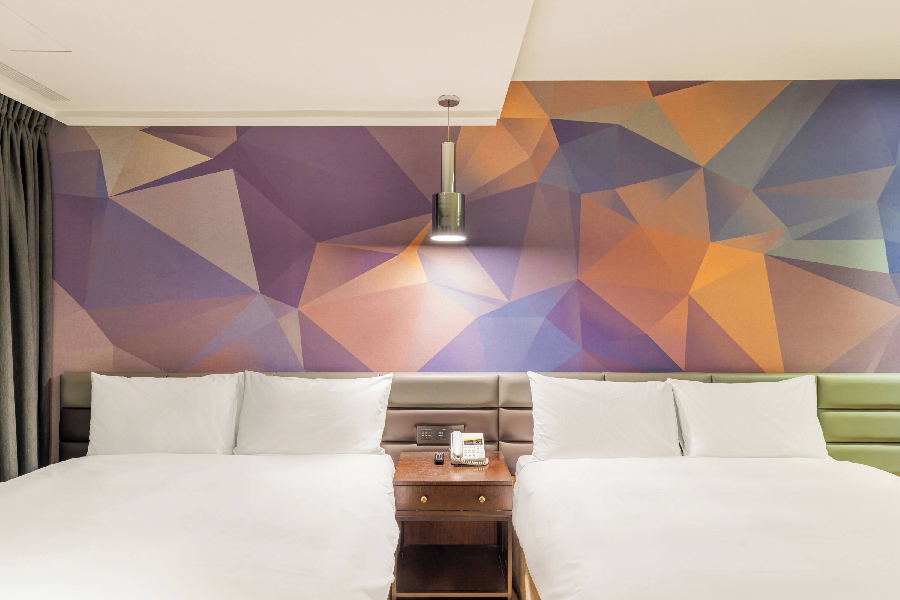 A hotel room with two beds, a nightstand with a phone, and a geometric-patterned wall.