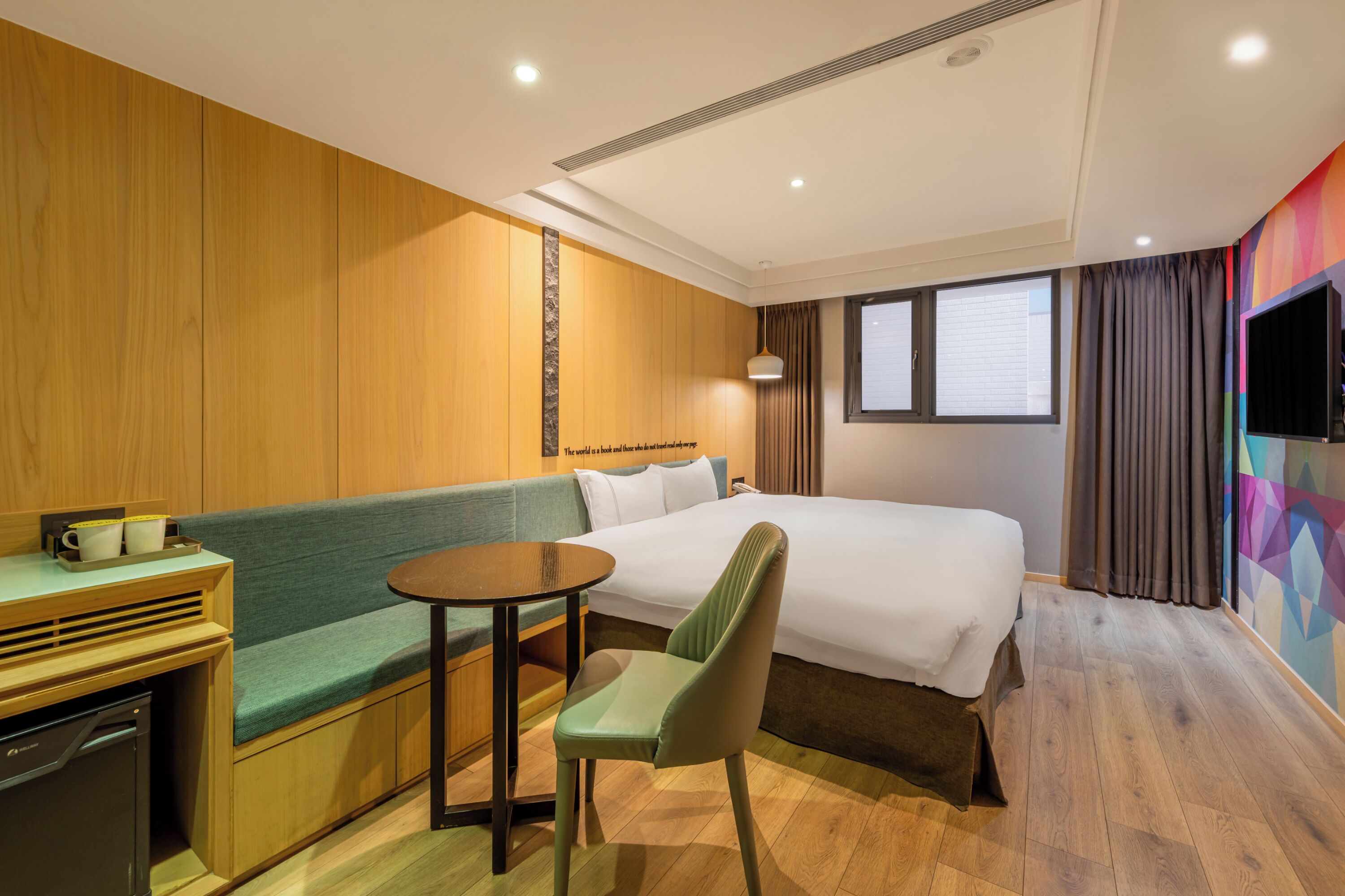 A hotel room with a bed, a green sofa, a small table, and a chair.