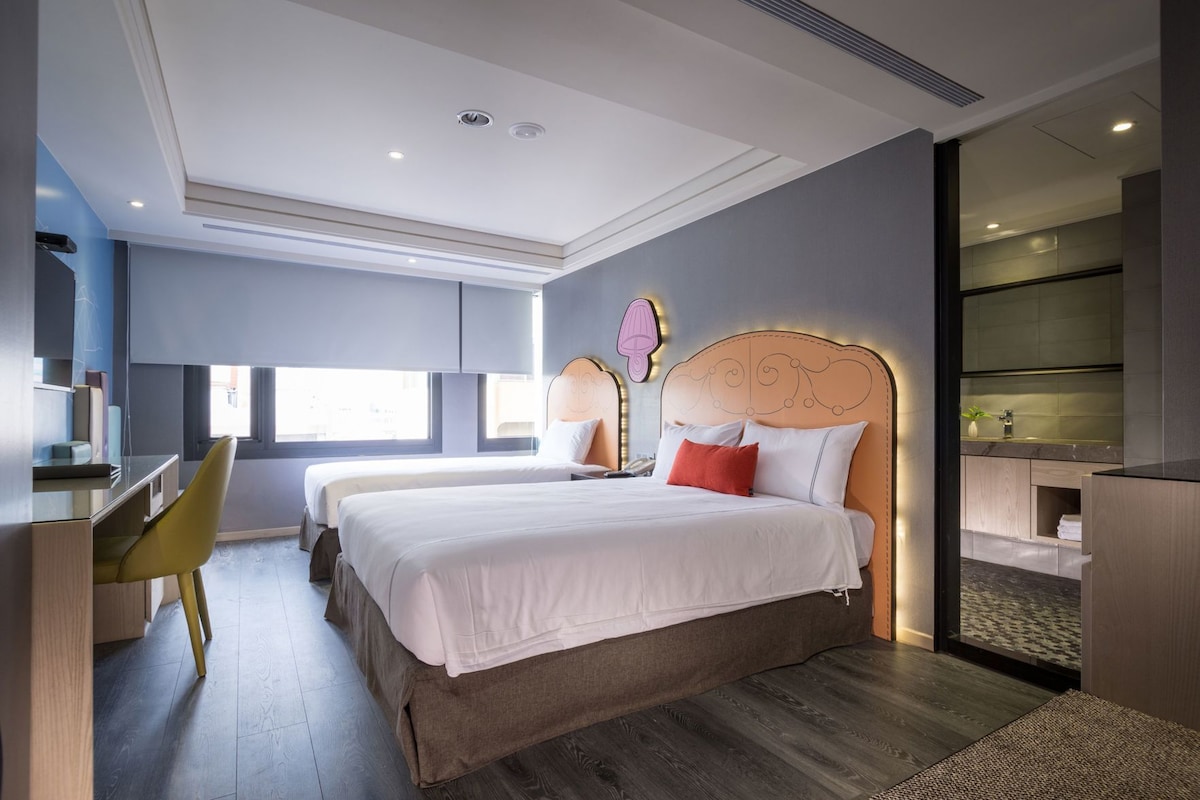 A modern hotel room with two beds, a desk, and a chair.