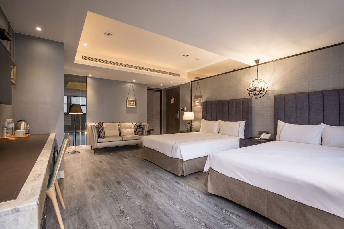 A modern hotel room with two beds, a sofa, a desk, and a dining area.