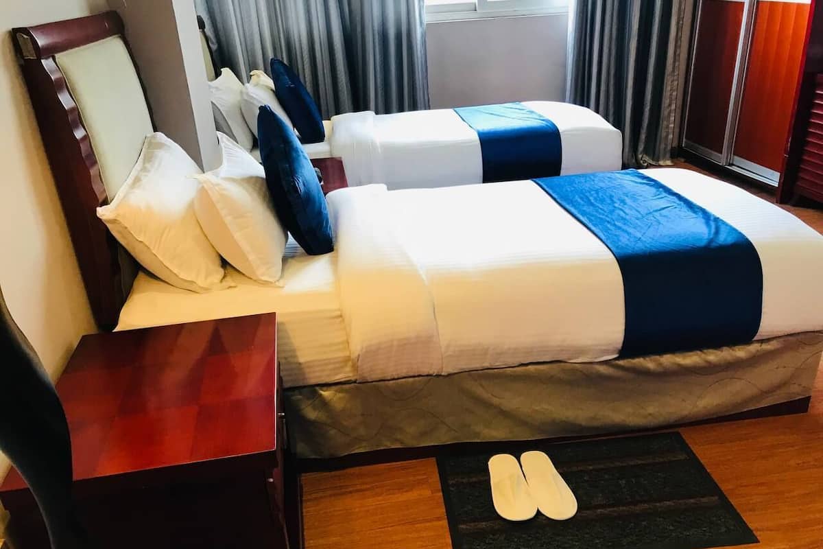 Habitación de hotel con cama, mesita de noche y un par de zapatillas en el suelo.