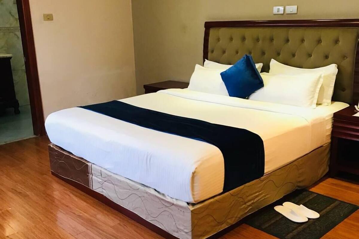 Una cama bien hecha con estructura de madera, cabecera y colcha de color oscuro.