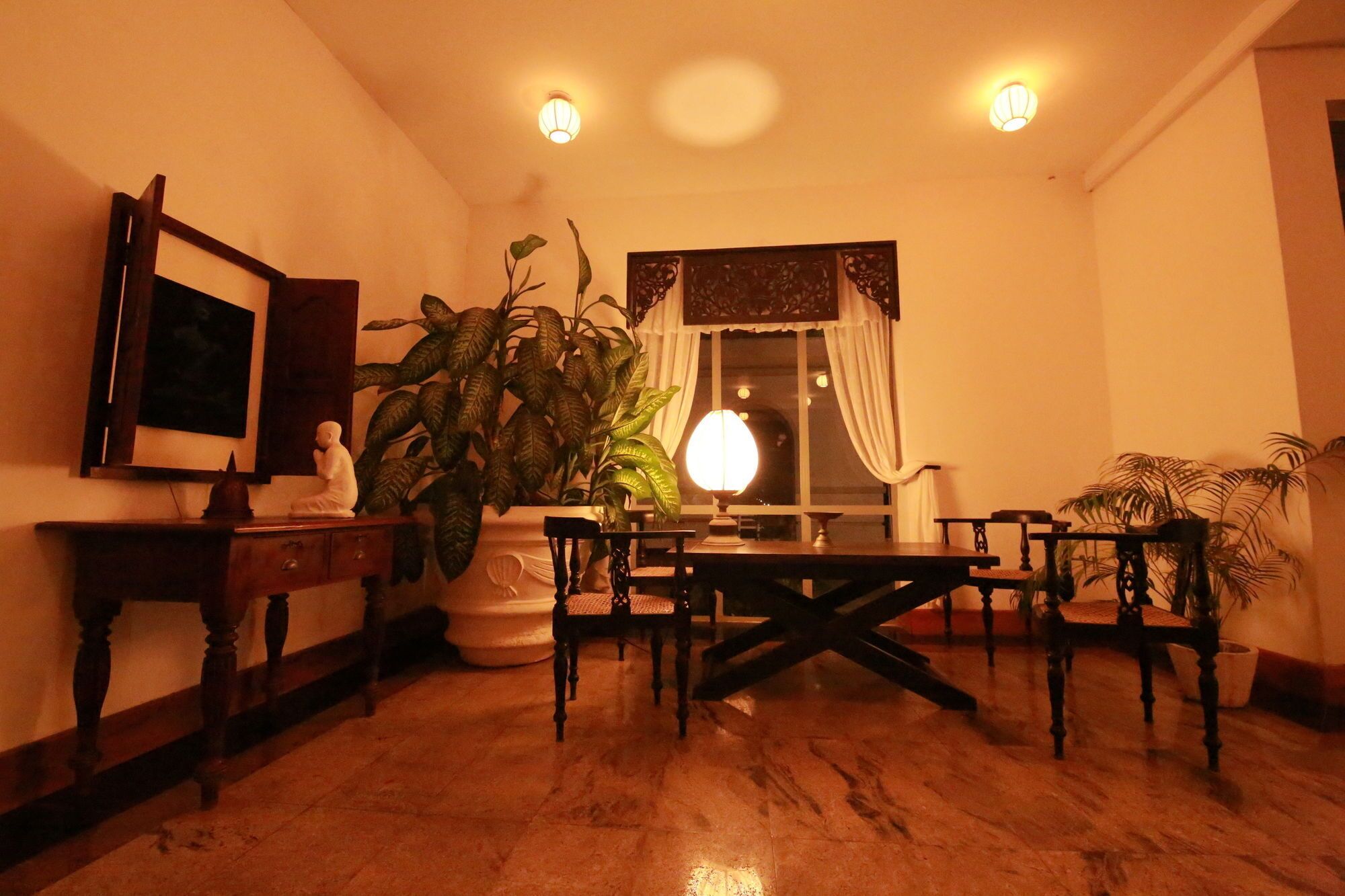 A dining area with a table and chairs, a potted plant, and a wall-mounted light fixture.