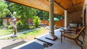 Ein überdachter Außenbereich mit einer Statue, Holzsäulen und Lounge-Stühlen.