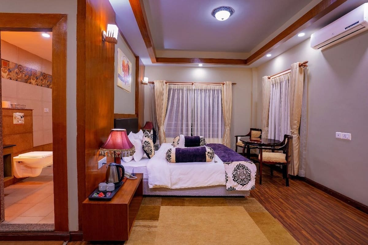 A hotel room with a bed, bedside table, lamp, and a window with curtains.