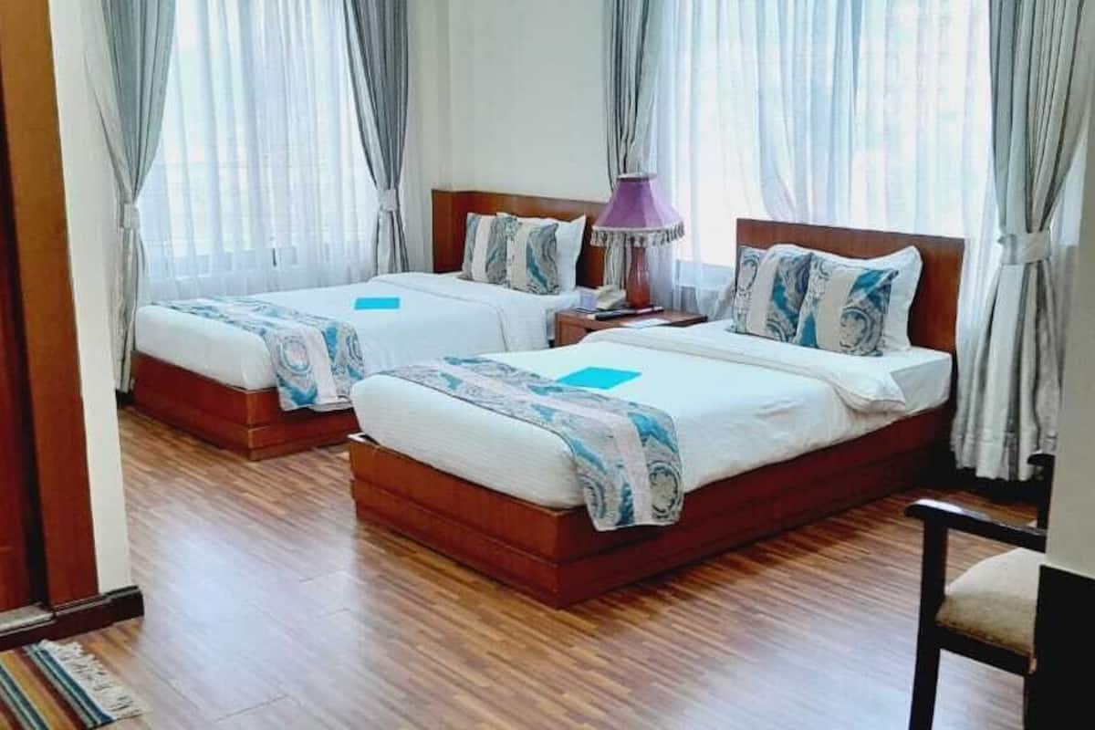 A hotel room with two beds, wooden flooring, and a door.