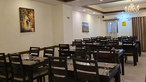 Un comedor espacioso con varias mesas y sillas, una araña de cristal y obras de arte en las paredes.