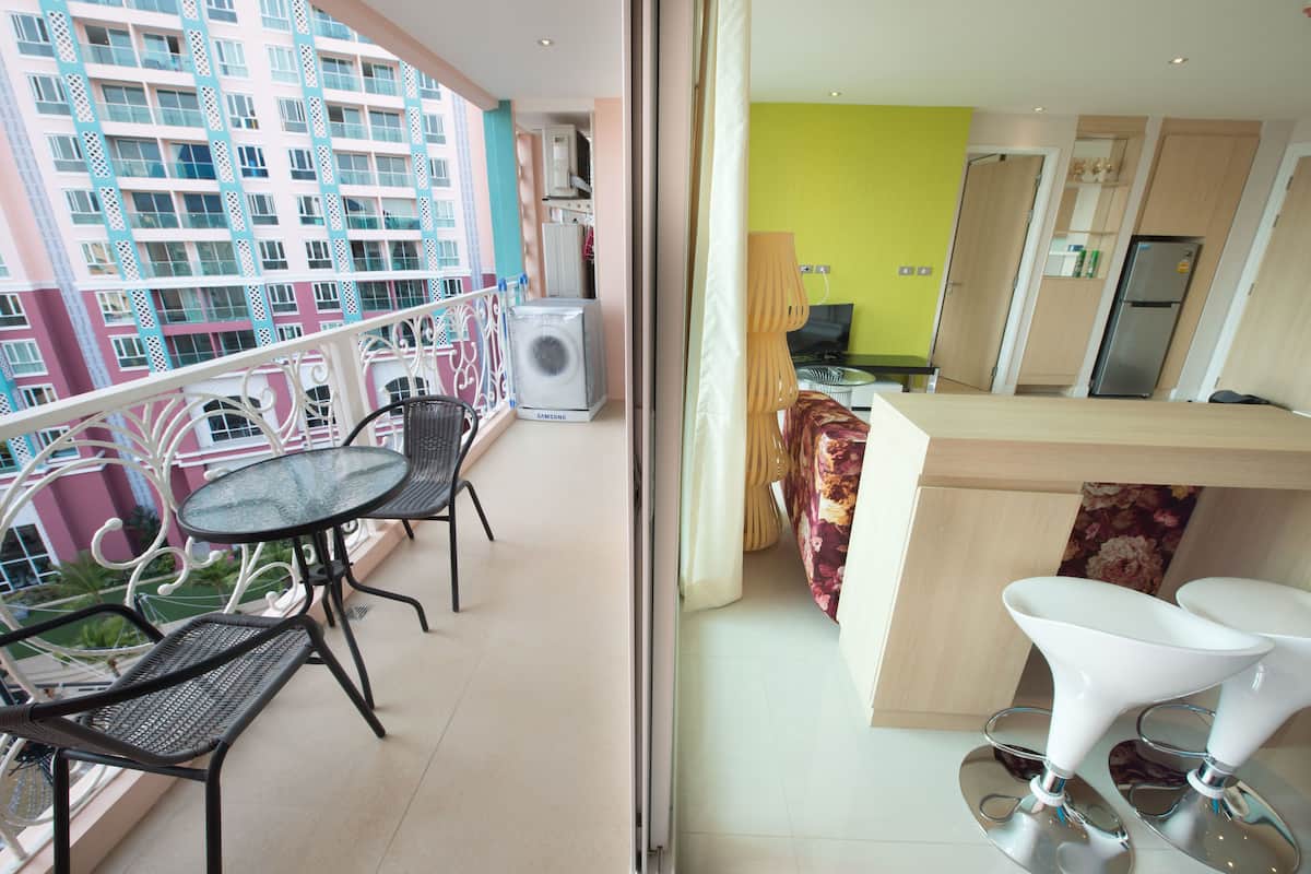 Un balcon avec une table et des chaises, un coin cuisine avec un réfrigérateur, et une vue sur un immeuble doté de balcons.