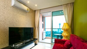 A modern living room with a flat-screen TV, red sofa, and a large window offering a city view.