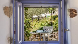 Una ventana pequeña con vistas a un jardín, una mesa y sillas afuera.