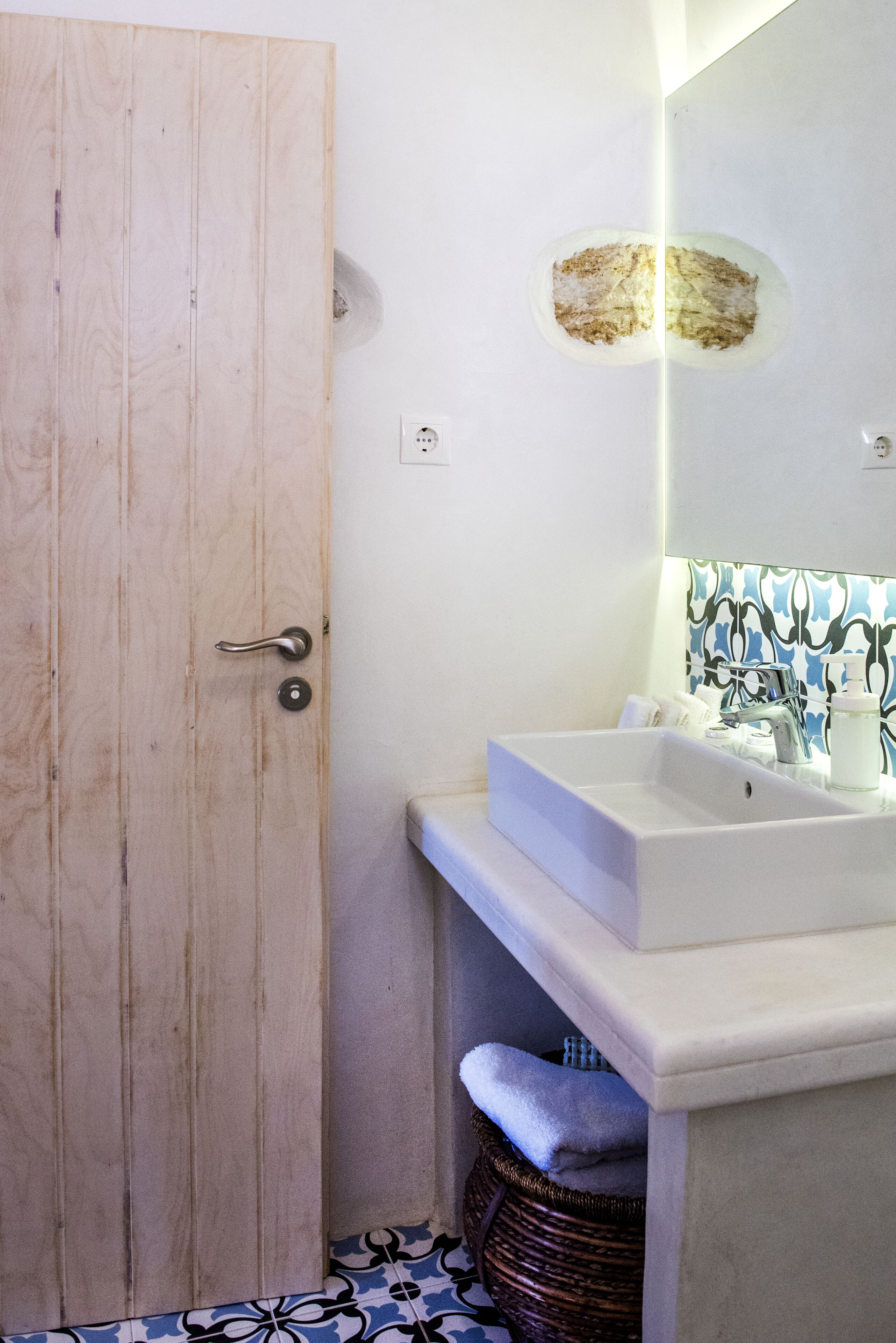 A bathroom with a wooden door, a white sink, a mirror, and a patterned tile backsplash.