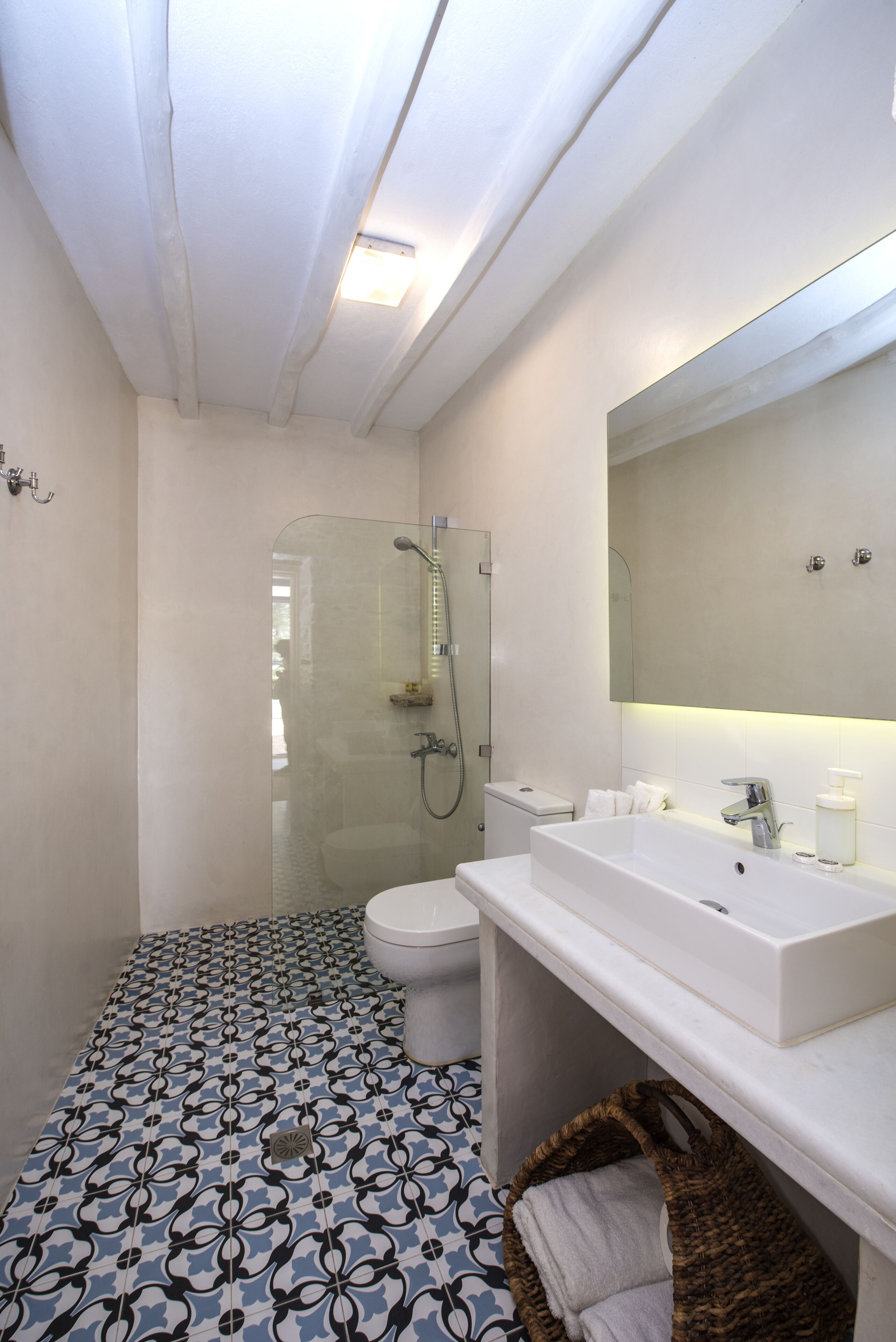 A bathroom with a glass-enclosed shower, a white sink, and patterned floor tiles.