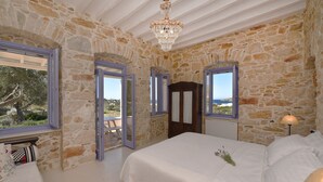Un dormitorio con paredes de piedra, una cama grande y vista al mar.