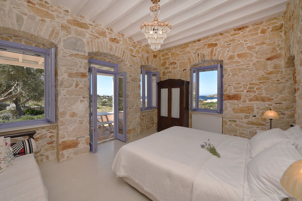 A bedroom with stone walls, a large bed, and a view of the sea.