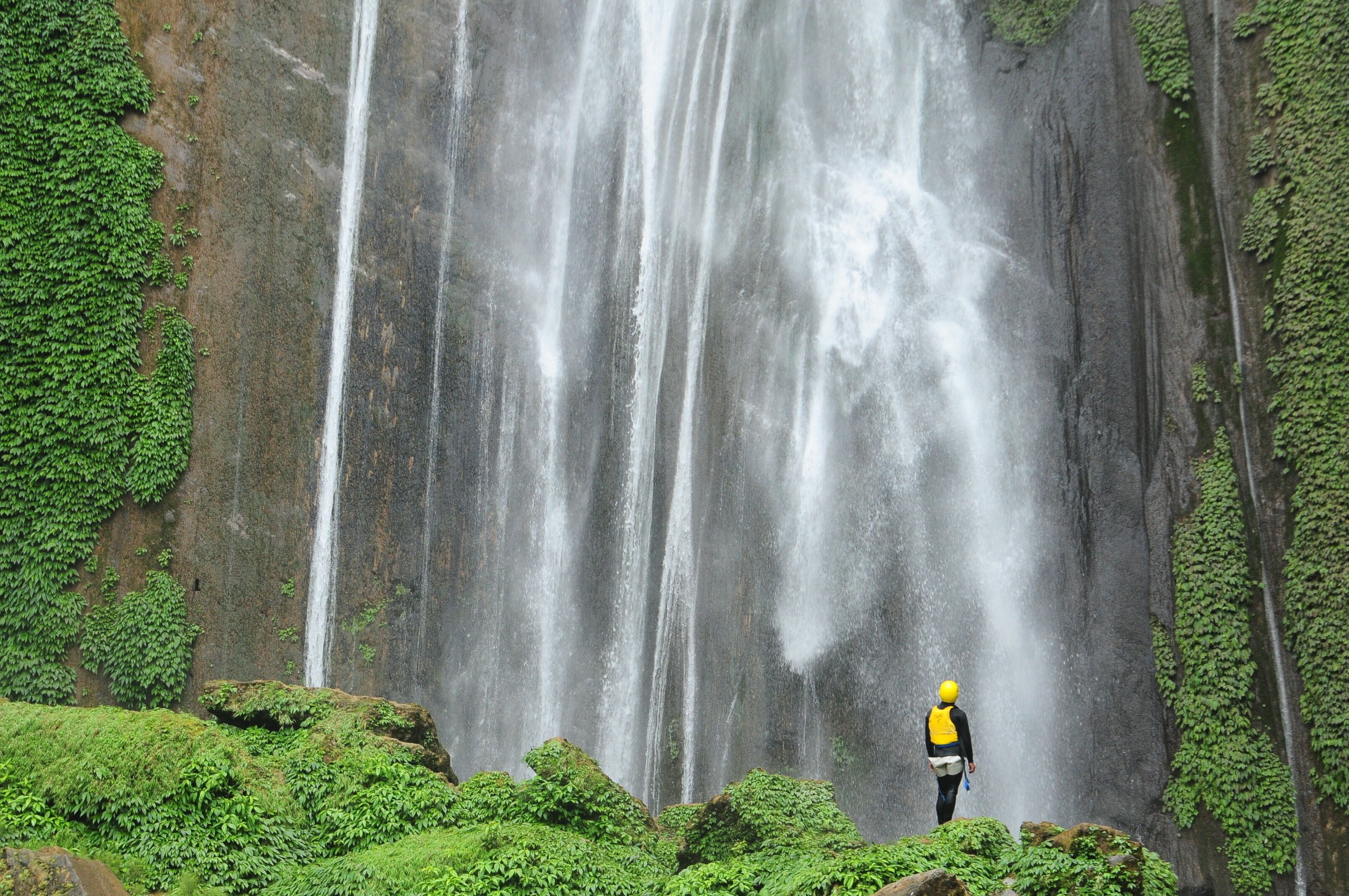 Una cascada con una persona que lleva un casco amarillo de pie frente a ella.