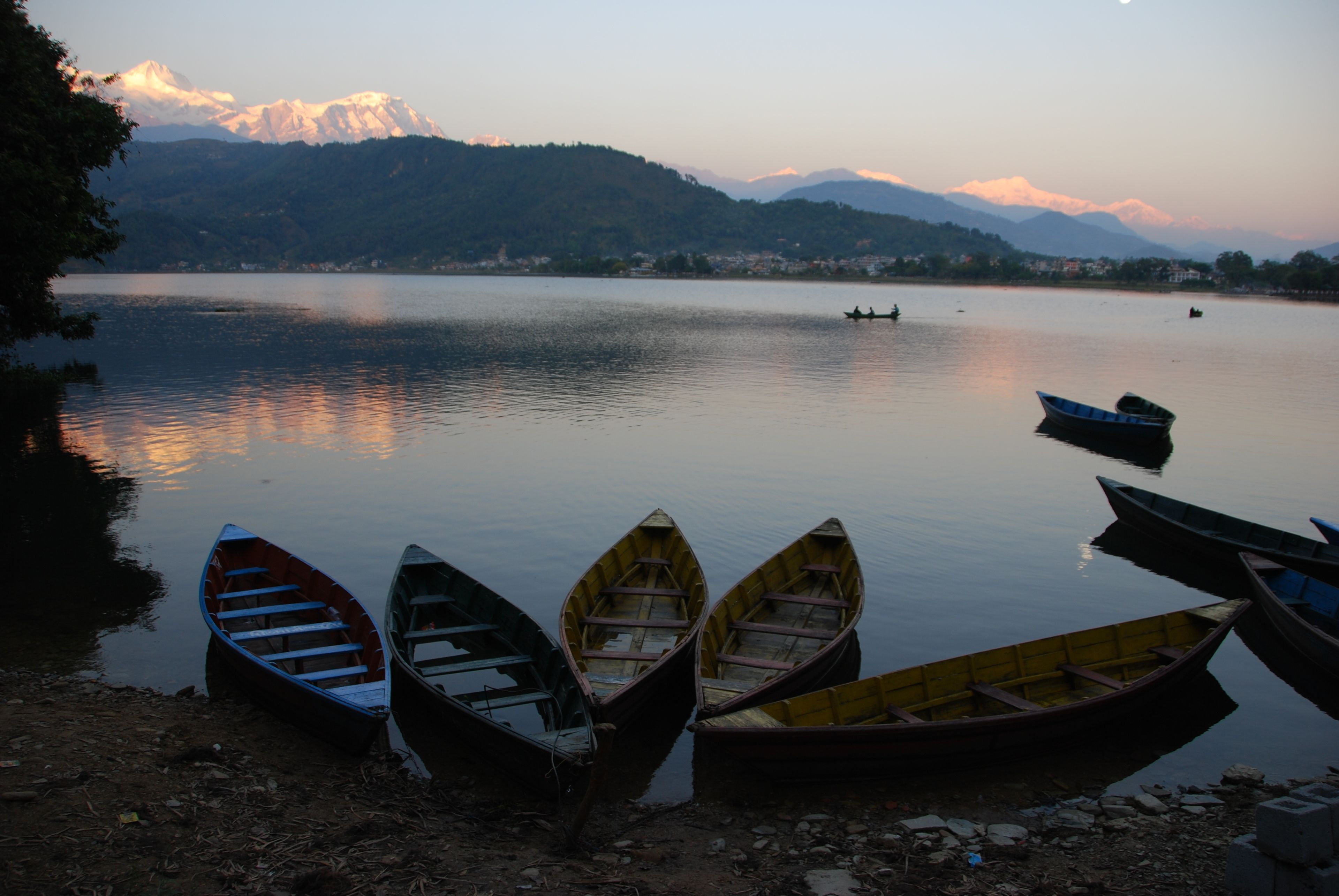 A calm lake with several boats docked on the shore, surrounded by mountains in the background.