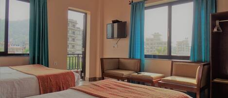 Habitación de hotel con dos camas, un televisor montado en la pared y un balcón con vistas a la ciudad.
