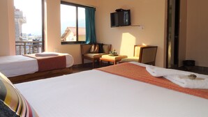 A hotel room with two beds, a TV, a window with curtains, a small table, and a chair. - Hotel Karuna (Pokhara)