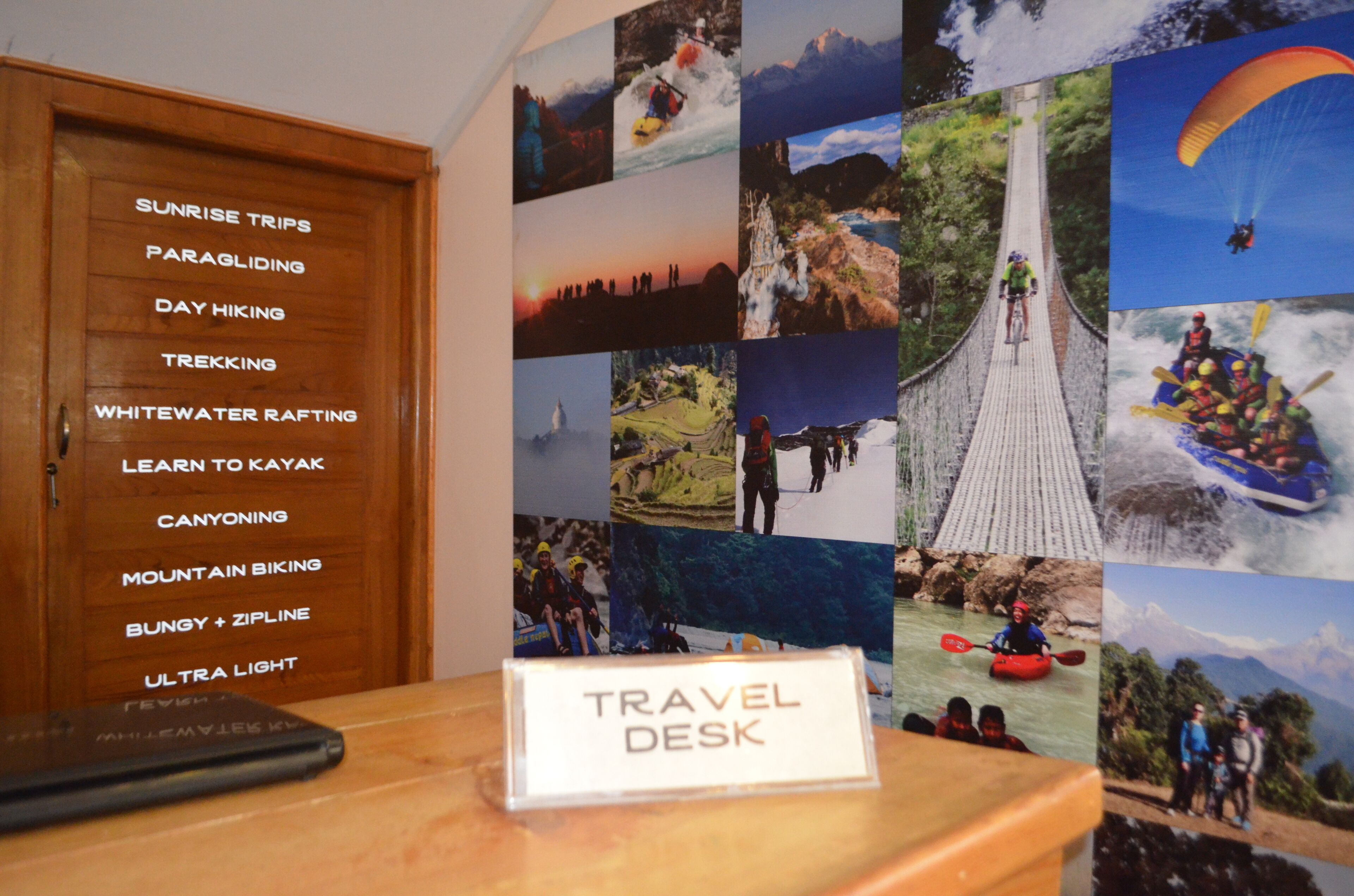 A travel desk with a sign labeled "TRAVEL DESK" and a wall with various adventure photos.