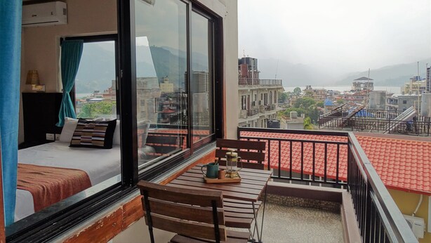 A balcony with a bed, a table with a lantern, and a view of a cityscape. - Hotel Karuna (Pokhara)