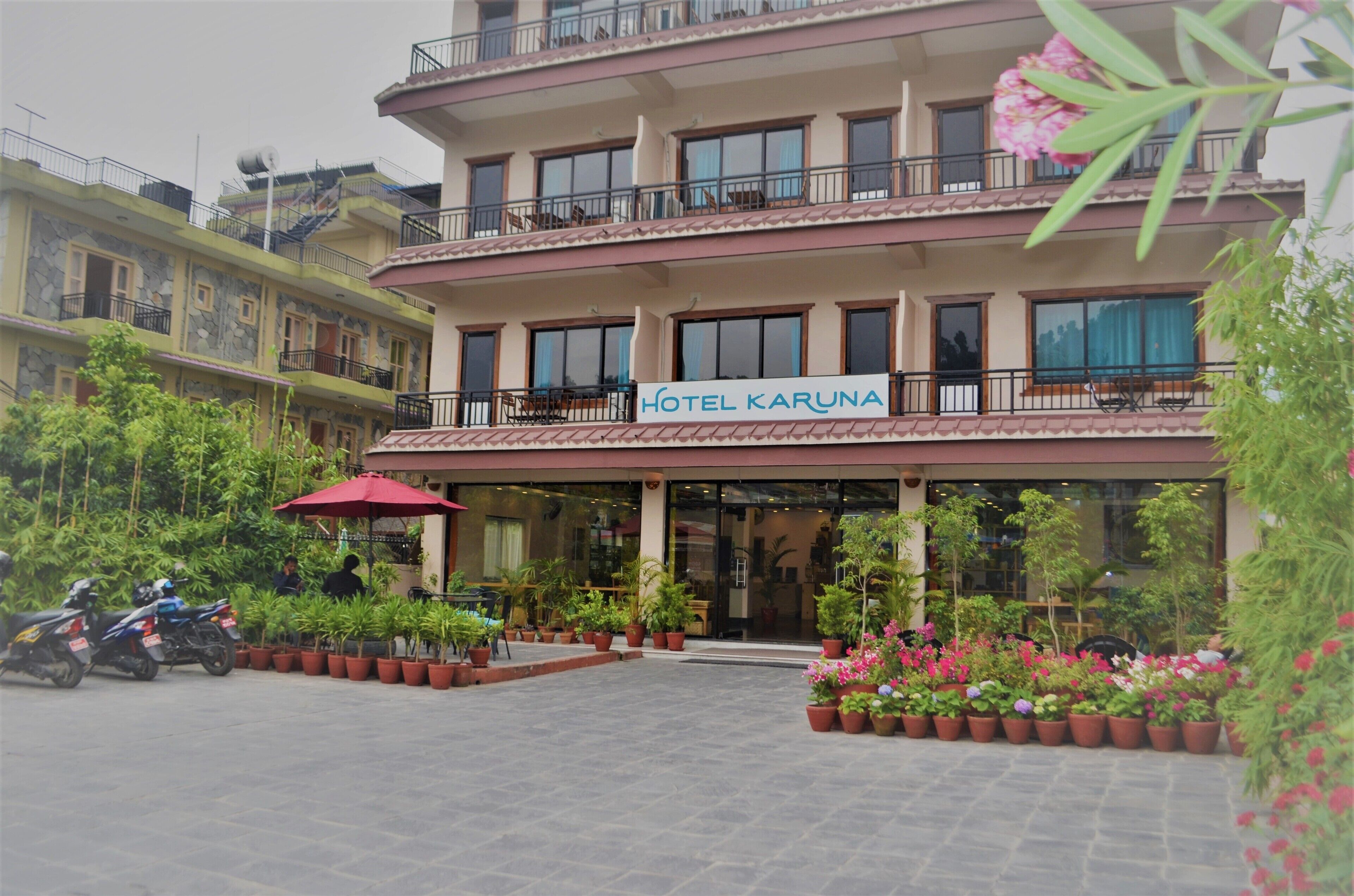 A multi-story hotel with balconies, a sign reading "Hotel Karuna," and potted plants in the courtyard.