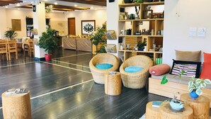 A spacious lobby with a reception desk, wicker chairs with blue cushions, wooden side tables, and a variety of decorative items on shelves. - Hotel Karuna (Pokhara)