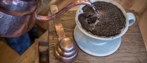 Una tetera de cobre vertiendo líquido en una taza de cerámica blanca sobre una mesa de madera.