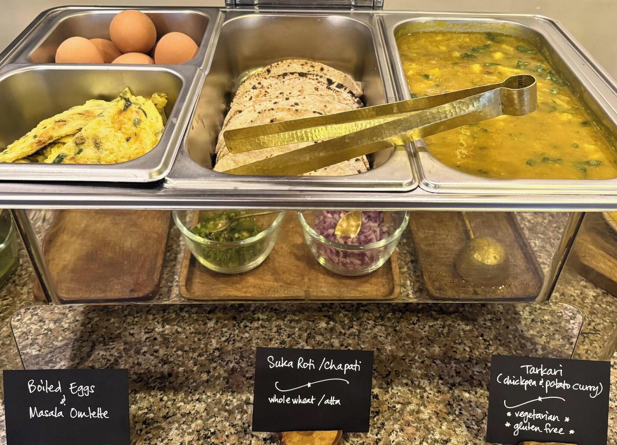 Un buffet proposant différents plats, chacun étant clairement identifié, notamment des œufs durs, une omelette masala, du Suka Roti/Chapati et du Tarki (un curry de poulet et de pommes de terre).