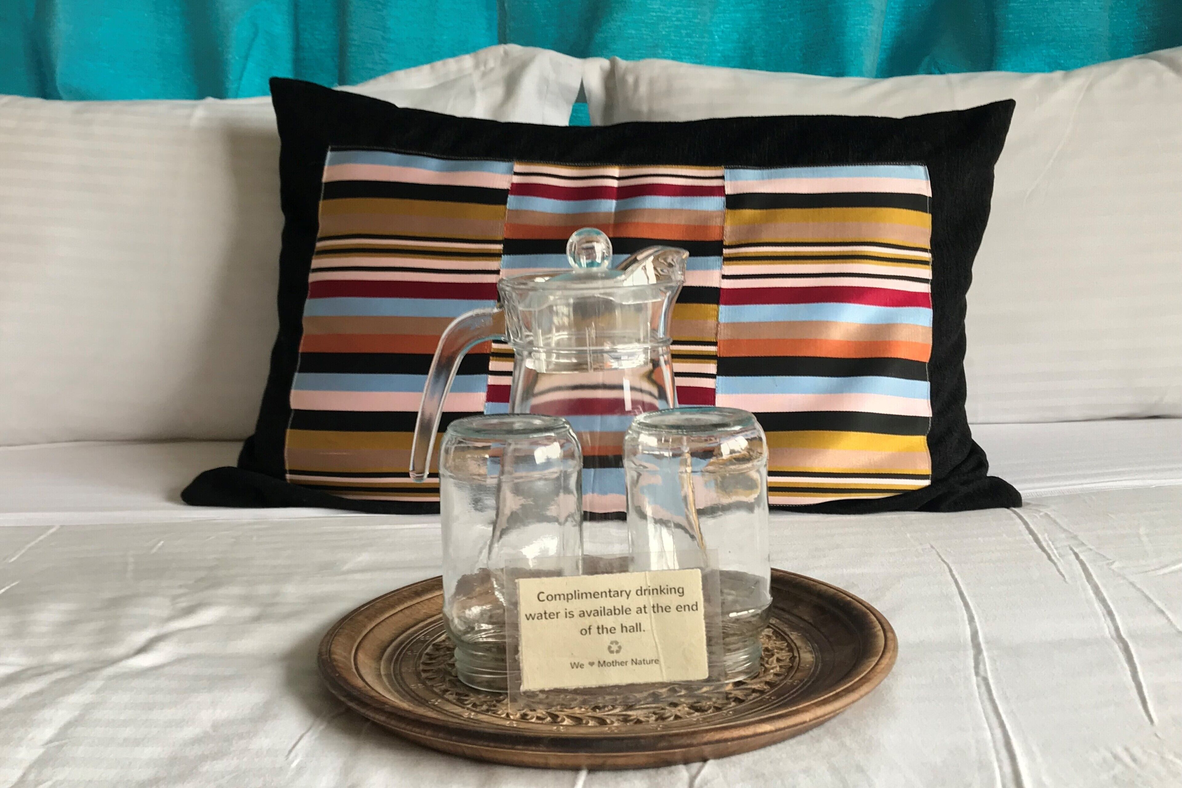 A glass pitcher and two glass carafes on a tray with a sign indicating complimentary water is available at the end of the hall.