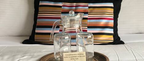 A glass pitcher and two glass carafes on a tray with a sign indicating complimentary water is available at the end of the hall.