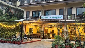 A hotel with a sign reading "HOTEL KARUNA". It features a balcony with a railing, potted plants, and a seating area with chairs and tables. - Hotel Karuna (Pokhara)
