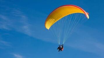 A person paragliding with a yellow and red parachute against a clear blue sky.