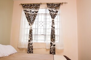 A bedroom with a bed, a window with patterned curtains, and a wall-mounted light fixture.