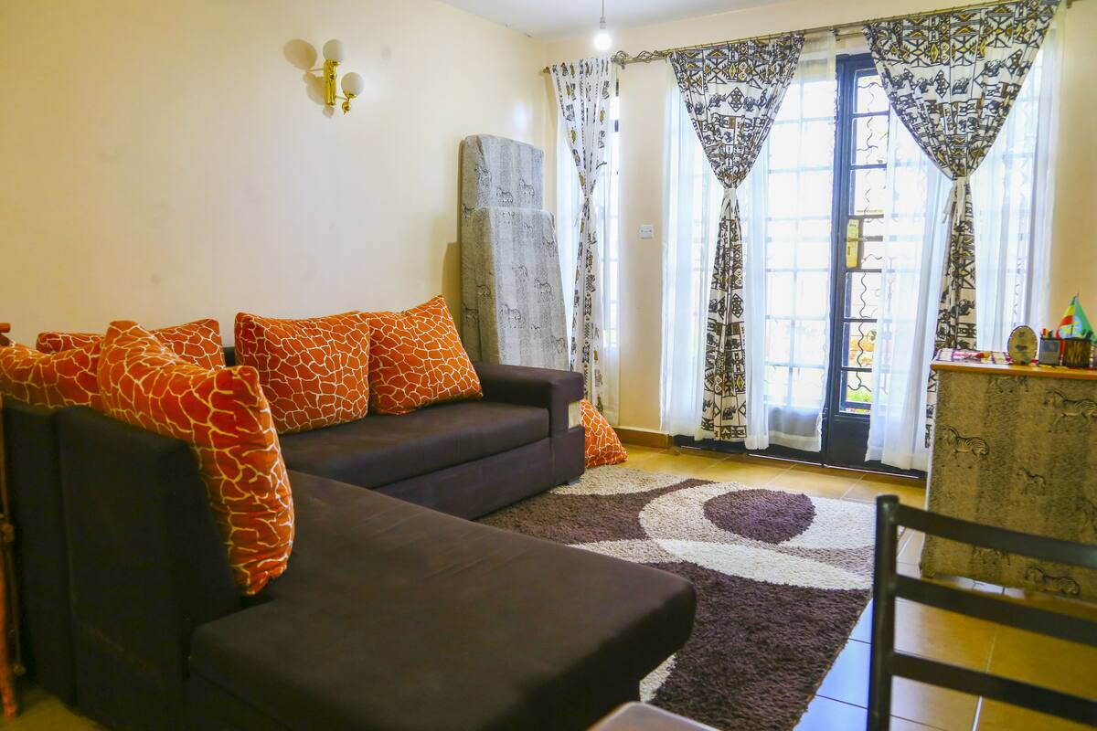 Ein Wohnzimmer mit einer Couch, gemusterten Kissen, einem Teppich und Vorhängen.
