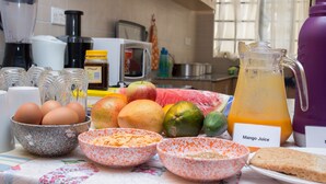 Eine Küchenarbeitsplatte mit verschiedenen Frühstücksangeboten, darunter Eier, Früchte und ein Krug Mangosaft.