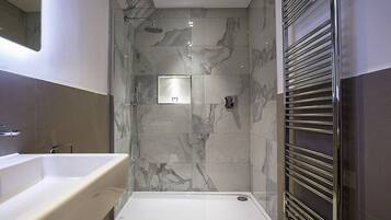 Un baño moderno con ducha a ras de suelo, bañera y zona de ducha con mampara de cristal.