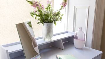 A desk with a laptop, a notebook, a vase with flowers, and a glass bottle.
