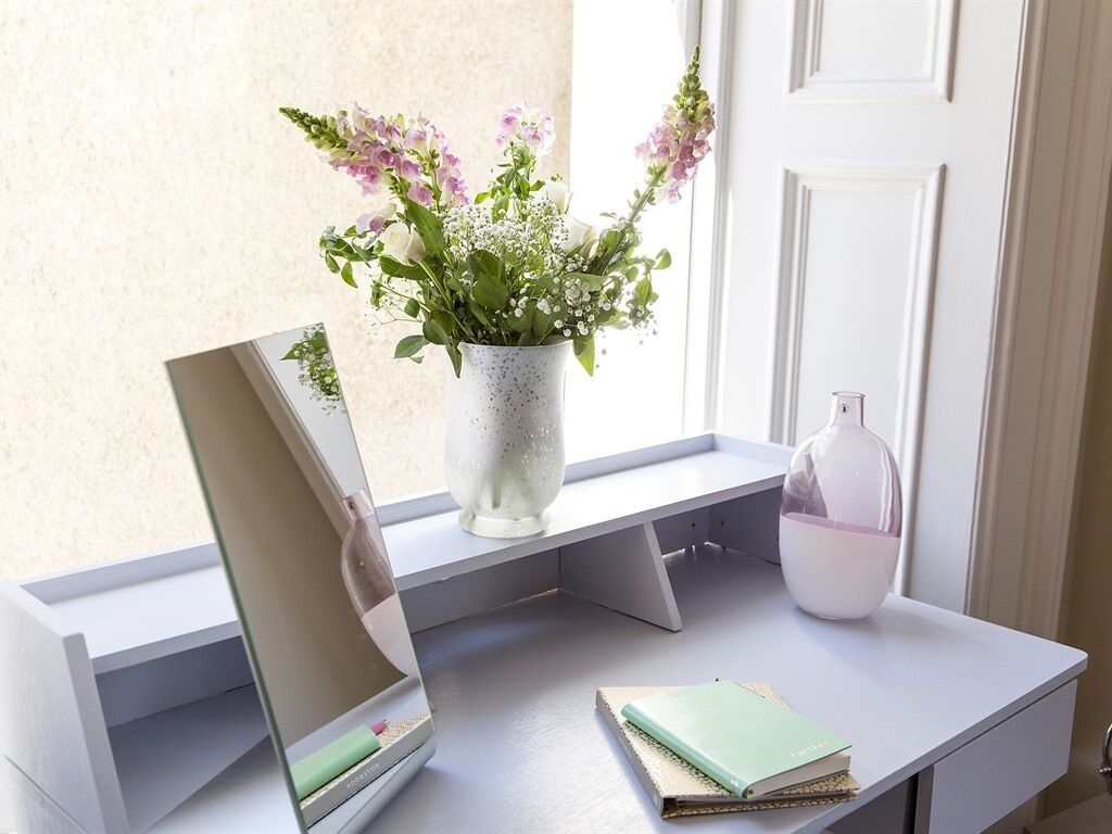 A desk with a laptop, a notebook, a vase with flowers, and a water bottle.
